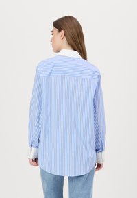 Camicia a maniche lunghe a righe blu e bianche con colletto tradizionale, dotata di polsini con bottone e orlo arrotondato.