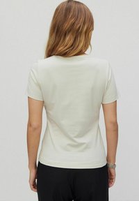 Kortærmet creme t-shirt i blødt stof, med rund halsudskæring og lige skæring i kanten, båret med sorte bukser.