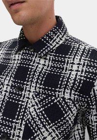 Czarna i biała koszula w kratkę, wykonana z teksturowanej tkaniny, z kołnierzykiem na guziki oraz czarnymi guzikami na kontrastowym tle.
