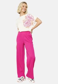 Witte T-shirt met korte mouwen en roze bloemenborduursel, gecombineerd met hoogwater, gestructureerde roze wijde broek en witte sneakers met marineblauwe accenten.