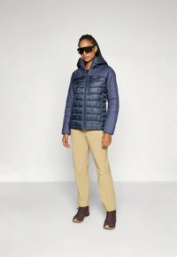 Tumši zila pūteņu jaka ar rāvējslēdzēju priekšpusē, ar šūtu tekstūru un kapuci. Kopā ar bēšām biksēm un brūnām pārgājienu zābakiem. Garas bizītes un saulesbrilles.