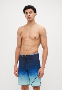 Pantaloni scurți de plajă cu un gradient albastru și verde, cu un talie întunecată, închidere cu șnur și logo pe lateral. Material din poliester cu o textură netedă.