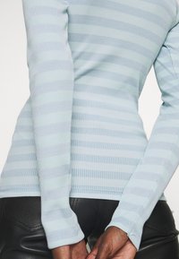 Helles blaues, geripptes Langarmshirt mit horizontalen Streifen in dunklerem Blau. Weiche Textur mit taillierter Passform und genähten Saumdetails.