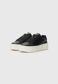 Baskets en cuir noir avec un bout arrondi, un laçage à l'avant et une semelle plate-forme blanche épaisse. Texture lisse avec un design minimaliste.