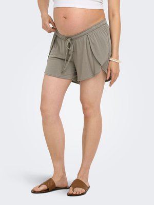 Femme enceinte portant un short de maternité gris clair avec taille à cordon, un top court blanc, un bracelet de perles et des sandales slides marron.