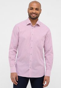 Camicia a maniche lunghe a righe rosse e bianche con colletto abbottonato. Presenta una tasca sul petto e accenti blu sui bottoni anteriori.