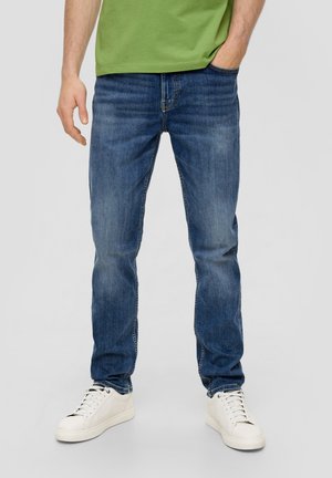 Jeans in denim blu con una vestibilità rilassata, caratterizzati da un design a gamba dritta e un leggero effetto sbiadito, abbinati a sneakers bianche con lacci.