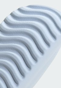 Nahaufnahme einer weißen strukturierten Oberfläche mit gleichmäßig verteilten, wellenförmigen Rillen, die ein sich wiederholendes Muster bilden.