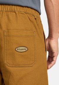 Shorts in cotone marroni con vita elastica e una tasca posteriore con un'etichetta circolare "Billabong" cucita in tonalità sabbia. Tessuto strutturato.