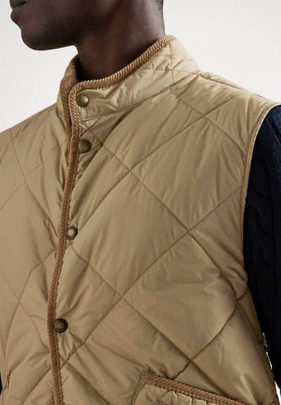 Beżowa pikowana kamizelka z wysokim kołnierzem, ozdobiona brązowym sztruksowym wyko�ńczeniem i zatrzaskami. Teksturowana tkanina z wzorem w diamenty.