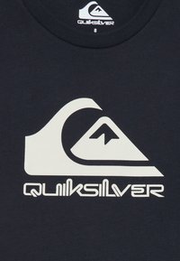 Jūrinės mėlynės T-shirt marškiniai, pagaminti iš medvilnės, su dideliu baltu "Quiksilver" logotipu, kuriame pavaizduota banga ir kalnas, lygia tekstūra ir apvaliu kaklu.
