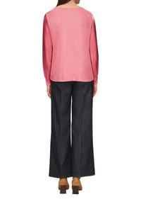 Langärmliges, rundhalsiges Oberteil aus weichem Rosa, kombiniert mit dunklen, weit geschnittenen Jeans. Das Model trägt hellbraune Blockabsatzschuhe.