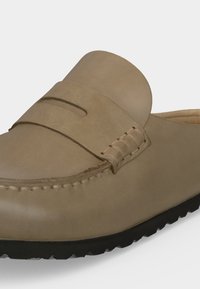 Μπεζ μοκασίνι τύπου slip-on με στρογγυλεμένη μύτη, ραμμένες λεπτομέρειες και μαύρη λαστιχένια σόλα με ραβδώσεις για καλύτερη πρόσφυση.