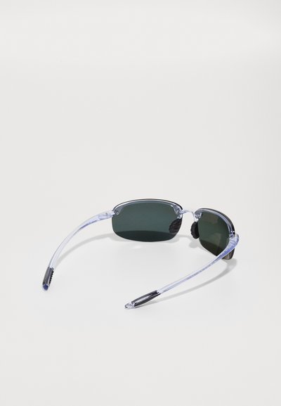 Sonnenbrille mit rechteckiger Form, gläsern mit grünem Farbton, klaren Kunststoffrahmen und schwarzen Gummihighlights an den Schläfen.
