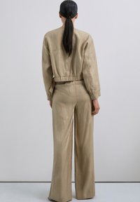 Chándal beige con un diseño texturizado, que presenta patrones de olas plateadas. La parte superior tiene una cintura elástica corta y los pantalones son de pierna ancha.