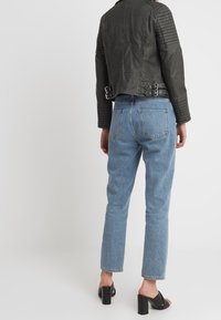 Czarna skórzana kurtka motocyklowa z karbowanymi ramionami i klamrami; jasnoniebieskie dżinsy z wysokim stanem; czarne sandały na słupku z odkrytymi palcami.