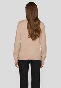 Beiger Pullover aus strukturiertem Strickstoff mit langen Ärmeln und rundem Ausschnitt, kombiniert mit schwarzer Hose, Rückenansicht.