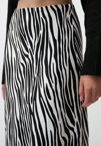 Jupe noir et blanc avec un motif rayé zèbre. Le tissu est lisse avec un design fluide, mettant en valeur une taille cintrée et une texture douce.