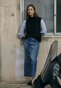 Pull noir sans manches sur une chemise bleu clair, associé à une jupe en denim taille haute avec des boutons sur le devant.