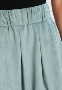 Ljusblå, mjuk tygkjol med bred elastisk midjeband och veck; texturen verkar slät och liknar mocka.