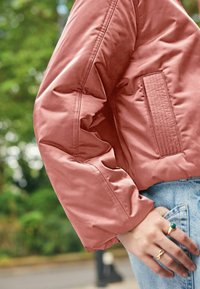 Krátka ružová puff jacket s prešívanou textúrou, skráteným dizajnom a detailom bočných vreciek. Ľahká tkanina s hladkým povrchom.