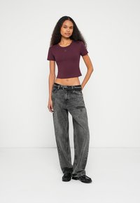 T-shirt curta de cor bordô com mangas curtas, combinada com jeans cinzentos escuros de corte largo, acentuados com um cinto preto e sapatos pretos.