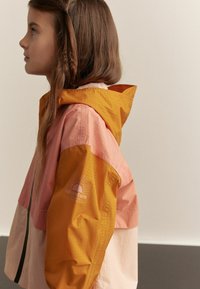 Färgglad vindjacka med paneler i orange, rosa och krämfärgad. Texturerad tyg med logotypdetalj på ärmen och huva.