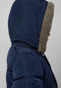 Marineblauwe gevoerde jas met een capuchon en een grijze fleece voering, ritssluiting en een gequilt textuur op het lijf.