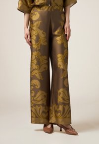 Braune Satin-Hosen mit weitem Bein, die ein goldenes Blumenmuster aufweisen, sowie einer glatten Textur und einem Saumfinish. Kombiniert mit braunen gewebten Absatzschuhen.