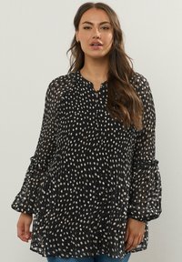 Svart genomskinlig blus med vita prickar, plisserad design, rund halsringning och trumpetärmar. Texturerad tyg ger djup till looken.
