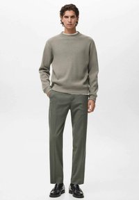 Suéter de punto en gris claro, diseño de cuello redondo combinado con pantalones verde oscuro. El modelo lleva zapatos negros, mostrando un ajuste relajado y una textura suave.