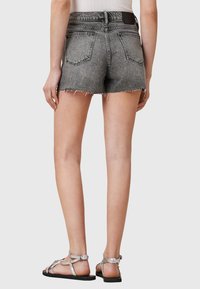 Shorts en denim gris avec un ourlet effiloché, cinq poches et une étiquette en cuir à l'arrière. Portés avec des sandales à lanières argentées.