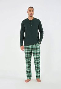 Sötétzöld, hosszú ujjú henley felső három gombbal, zöld kockás pizsamanadrággal párosítva, amely különböző zöld és fekete árnyalatokban pompázik.