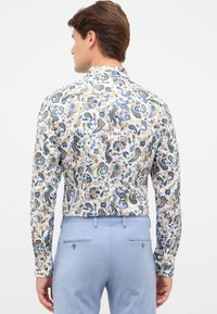 Langearmige shirt in het wit met multikleurige paisley- en bloemenpatronen. Getailleerd ontwerp met een standaard kraag. Gecombineerd met lichtblauwe broek.