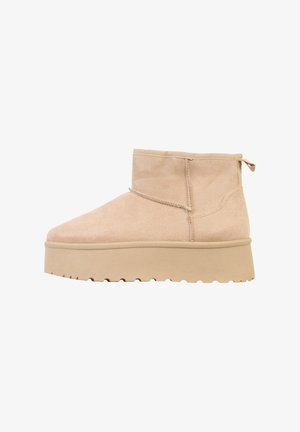 Bottines en daim beige avec un bout arrondi, une tige courte et une semelle plateforme épaisse et texturée. Elles sont dotées d'une languette de traction à l'arrière.