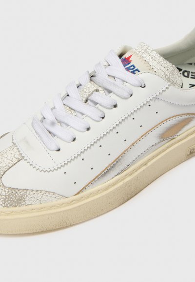 White leather sneaker with silver accents, textured toe cap, perforations along the sides, and white laces. Rubber sole and branded tongue.