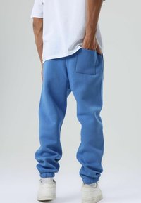 Blauwe joggingbroek met een ontspannen pasvorm, geribbelde boorden en een achterzak. Draagt een wit T-shirt en is gecombineerd met witte sneakers.