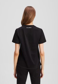 T-shirt in cotone nero con maniche corte, colletto rotondo e un logo sottile stampato in bianco sulla parte superiore della schiena. Tessuto morbido, vestibilità comoda.