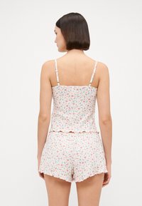 Pajamas u dva dijela s cvjetnim uzorkom izrađeni od lagane tkanine; sadrže uski top s volančićem i kratke hlače s valovitim rubovima.
