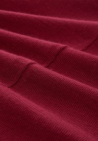 Burgunderfarbener Stoff mit einem texturierten, wellenförmigen Muster, das weiche, dicke Fasern in einer drapierten, gefalteten Anordnung zeigt.