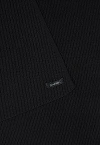 Tissu tricoté côtelé noir plié avec une petite étiquette rectangulaire de la marque Calvin Klein cousue sur le bord inférieur.