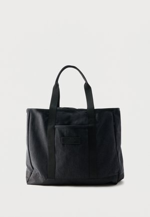 Sac fourre-tout rectangulaire noir avec deux poignées et une poche avant, fabriqué en tissu avec une base semblable à du cuir.