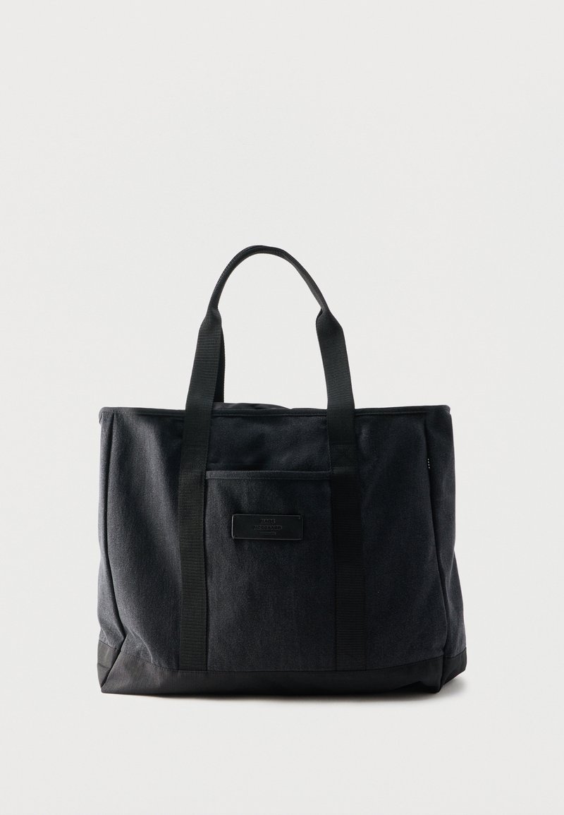 Sac fourre-tout rectangulaire noir avec deux poignées et une poche avant, fabriqué en tissu avec une base semblable à du cuir.