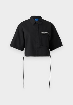 Juoda trumpa susegama susiaurinta palaidinė su trumpomis rankovėmis, kairėje krūtinėje kišenė su "KARL LAGERFELD JEANS" logotipu ir raišteliais apačioje.