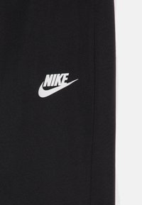 Pantalons de jogging Nike en tissu noir avec un logo blanc et une texture lisse. Le design présente une silhouette simple sans motifs supplémentaires.