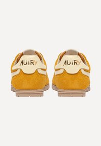 Sneakers in suede giallo con accenti beige, caratterizzati da una finitura testurizzata e logo "AUTRY" in rilievo sul tallone. Suola in gomma.