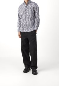 Vit långärmad skjorta med knäppning och intrikata svarta och grå mönster, kombinerad med löst sittande svarta byxor och svarta skor.