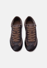 Ζευγάρι καφέ και σκούρα παπούτσια Vans με υφή γούνας, με καφέ κορδόνια, σε λευκό φόντο, φωτογραφημένα από ψηλά.