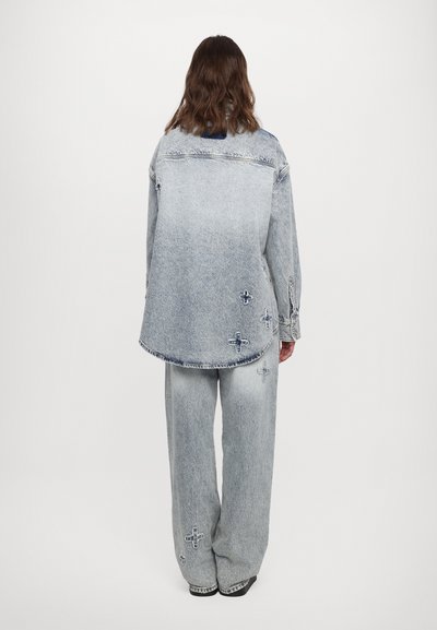 Šviesiai skalbtas denimo marškiniai ir kelnes su laisvu siluetu. Marškiniai pasižymi šiek tiek kreivu apvadu ir dekoratyvine tamsios siūlės kryžmine siuvinėjimu.