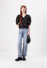 Maglione nero a maglia con motivi a cuore bianchi, maniche a palloncino corte, abbinato a jeans azzurri a vita alta e scarpe con plateau nere.